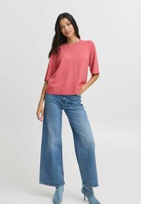 Roze kortemouwen sweater met een ronde hals, gecombineerd met wijde blauwe denim jeans en lichtblauwe hakken. Gladde textuur en relaxte pasvorm.