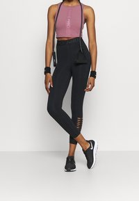 Czarne legginsy z wysokim stanem z wycięciami na łydkach, zestawione z krótką fioletową koszulką Nike Pro i czarnymi butami sportowymi.