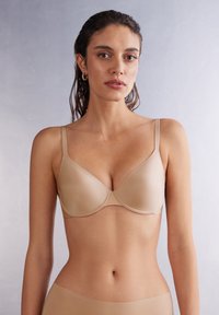 Beige seamless bra with adjustable straps and underwire, featuring smooth microfiber fabric and a rounded cup design.