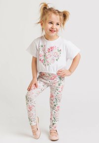 Biała bluzka z krótkim rękawem w kwiatowy wzór, połączona z jasnymi, kwiatowymi legginsami. Całość uzupełniają jasnoróżowe buty.