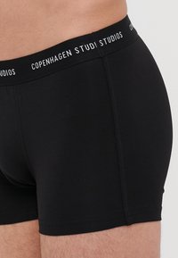 Svart bomullsboksershorts med en glatt tekstur, med en bred svart elastisk midjebånd med hvit trykt merkevare.