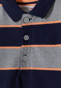 Grå polo med marinblå och orange horisontella ränder. Tre grå knappar vid kragen, med en liten broderad logotyp nära fållen.