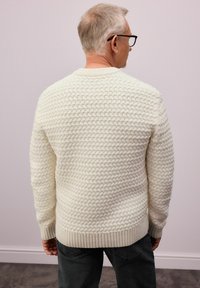 Cremfarbener Strickpullover mit einem strukturierten Muster sowie geripptem Kragen und Bündchen. Der Rücken ist unifarbig und hat einen lässigen Schnitt.