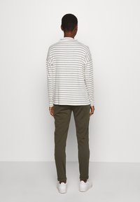 Pasiasta, długosleeve'owa koszula w białym i szarym kolorze, połączona z oliwkowymi spodniami. Białe sneakersy dopełniają stylizację. Prosty, casualowy design.
