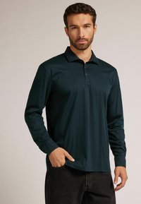 Dunkelgrünes Langarm-Polohemd aus glattem Stoff, mit Kragen, Knopfleiste mit drei Knöpfen und lockerer Passform. Keine sichtbaren Muster.