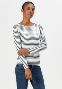 Haut à manches longues rayé en blanc avec des rayures noires, doté d'un col rond et d'une silhouette ajustée, associé à un jean en denim bleu.