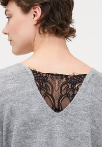 Gray sweater with a V-neck and black lace detailing at the back. Soft texture, relaxed fit, and intricate lace pattern add contrast.