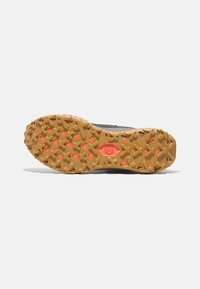 La suela de la zapatilla deportiva gris presenta una suela de goma texturizada con acentos en naranja y un patrón de rodadura geométrica para mejor agarre.