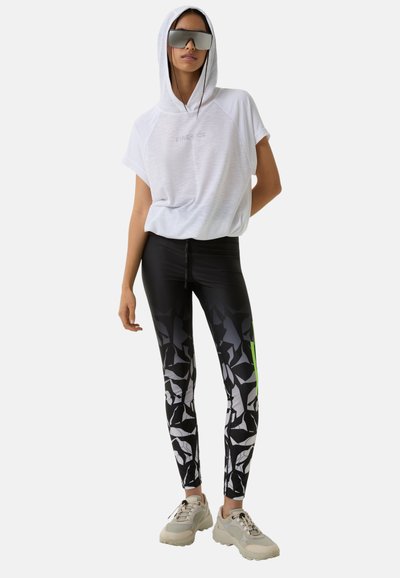White hooded short-sleeve top with "FIRE & ICE" text. Black leggings with abstract white and gray pattern, accented with neon green. Beige sneakers.