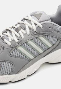 Baskets de sport grises en mesh et en daim, avec trois rayures gris clair, des lacets blancs et une semelle blanche texturée.