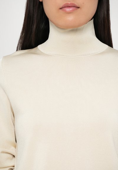 Bežs turtleneck top, kas izgatavots no ribotas adīkšanas auduma, ar pieguļošu dizainu un augstu apkakli. Gluda tekstūra ar minimālu detalizāciju.