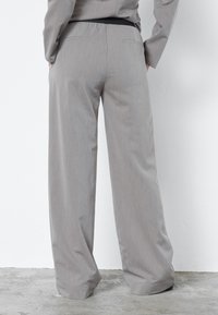 Szürke, széles szárú nadrág struktúrált anyagból, fekete gumis derékpánttal és két hátsó zsebbel. A szabás laza és áramló.