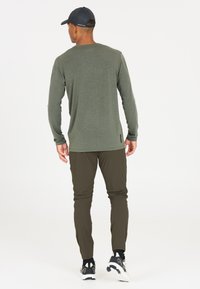 Langdurige mouw, olijfgroene top met een ronde halslijn, gecombineerd met strakke olijfgroene broeken en zwarte sneakers, met een eenvoudige achterkantweergave.