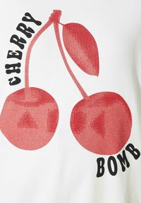 Vit T-shirt med grafisk tryck av röda körsbär och svart text "CHERRY BOMB." Körsbärsmotivet har en prickig struktur och en jämn yta på tyget.