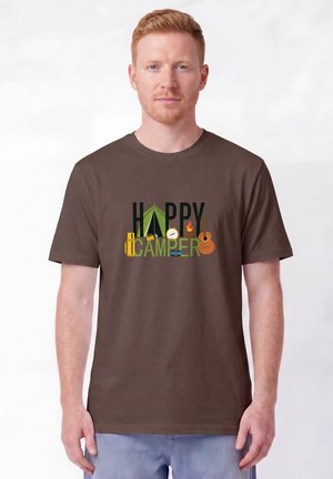 Homme à la peau claire et aux cheveux roux portant un T-shirt marron avec des icônes de camping et le texte "Happy Camper", debout sur fond blanc.