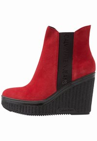 Czerwona zamszowa botka na koturnie, z fakturowaną czarną gumową podeszwą i czarną elastyczną opaską z napisem "Calvin Klein Jeans".