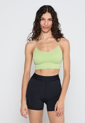 Limonkowozielony prążkowany krótki top na cienkich ramiączkach, zestawiony z wysokim stanem czarnych szortów. Miękka tekstura i dopasowany krój zwiększają komfort.