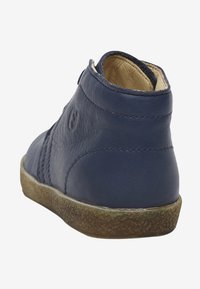 Zapato de cuero azul marino hasta el tobillo con superficie texturada, forma redondeada y suela de goma ligeramente desgastada. Presenta un sutil detalle de costura lateral.