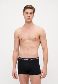 Schwarze Boxer Shorts mit einem elastischen Bund, auf dem "JACK & JONES" in weißer Schrift steht. Der Stoff wirkt glatt und eng anliegend. Das Modell ist oberkörperfrei.