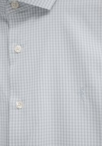 Camicia a quadri grigio chiaro e bianca con bottoni bianchi e logo ricamato sul petto raffigurante una persona che fa un colpo a golf.