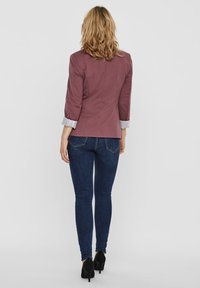 Bordowy żakiet z trzema-czwartymi rękawami, z paseczkowymi mankietami. W połączeniu z ciemnoniebieskimi wąskimi jeansami i czarnymi butami na wysokim obcasie.