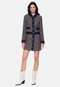 Tweed jacket and skirt set in navy, red, and white. Features a collared neck, gold buttons, and patch pockets. Worn with white ankle boots.