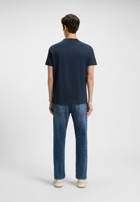 Una camiseta de manga corta de color azul marino con cuello redondo, combinada con unos vaqueros rectos de color azul claro y zapatillas beige. Diseño sencillo, sin patrones.