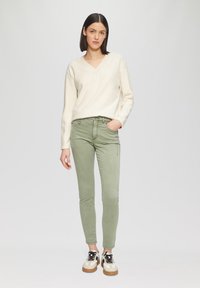 Lichtbeige v-hals trui gecombineerd met slim-fit, olijfgroene broek en witte sneakers met zwarte accenten. Eenvoudig ontwerp, geen zichtbare patronen.