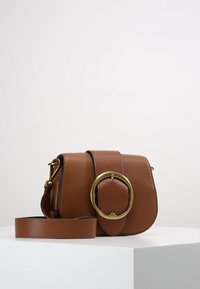 Brun läderhandväska med en rundad gul accent, texturerad yta och justerbar rem. Kompakt, med lock och magnetstängning.