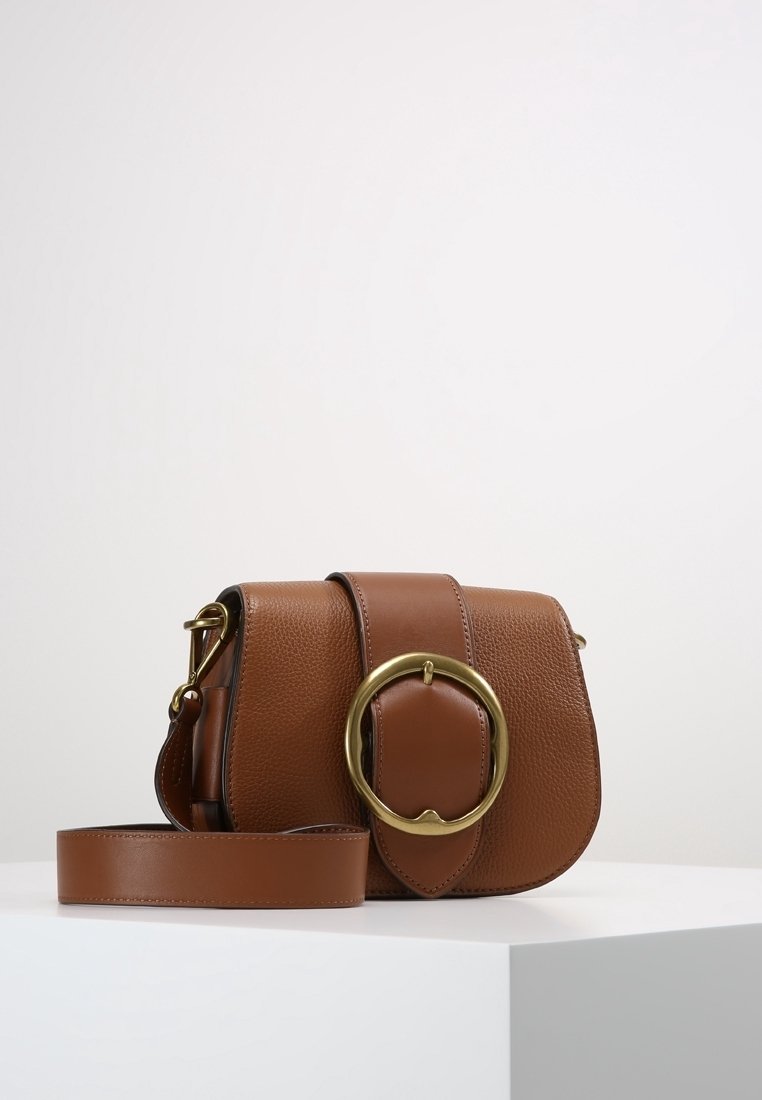 Brun läderhandväska med en rundad gul accent, texturerad yta och justerbar rem. Kompakt, med lock och magnetstängning.