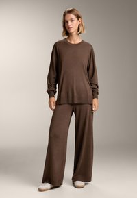 Barna kötött pulóver hosszú ujjakkal, széles lábú barna nadrággal párosítva. A szett laza szabású és sima textúrájú.