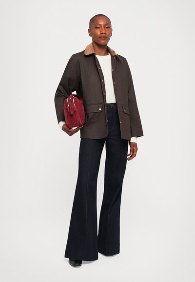 Brown waxed canvas jacket with tan corduroy collar, paired with high-waisted dark flared jeans and a maroon suede handbag.