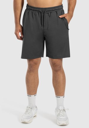 Grijze sportshorts met een elastische tailleband en trekkoord. Heeft zijzakken en een ruime pasvorm. Draag met witte sneakers en sokken.