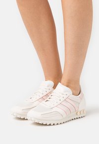 White athletic shoes with pink stripes, mesh and textile materials, rounded toe, cushioned sole, and textured accents on heel.