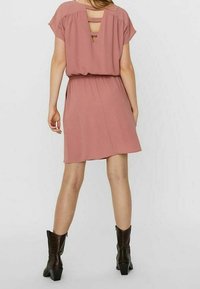 Růžová šaty v malinové barvě s V-zadním designem, krátkými rukávy, elastickým pasem a volným střihem, doplněné tmavě hnědými kotníkovými botami.