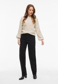Light beige, ribbed sweater with balloon sleeves paired with high-waisted, straight-leg black pants. Model wears black heeled boots.