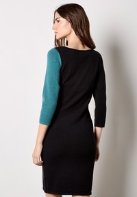 Figurbetontes Kleid mit schwarzem Oberteil und langärmligem türkisfarbenem Stoff, gefertigt aus weichem Strickmaterial, mit einem runden Ausschnitt und einem knielangen Saum.