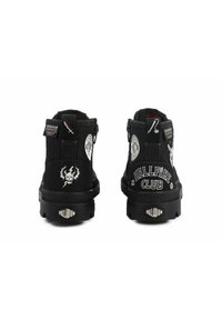 Bottes noires à la cheville en matériau textile, avec fermeture éclair et divers motifs graphiques blancs, y compris "HELLFIRE CLUB" et des designs de crânes.