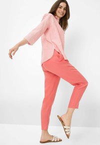 Koraalkleurige linnen broek gecombineerd met een roze en witte gestreepte blouse. De blouse heeft een ontspannen pasvorm en 3/4 mouwen. Beige instappers.