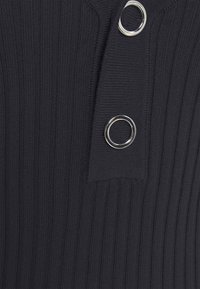 Top en tricot noir côtelé avec un col haut et deux accents circulaires en argent comme boutons, en tissu texturé et légèrement extensible.