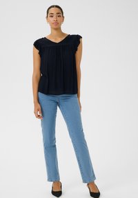 Blouse sans manches bleu marine avec des épaules froncées, décolleté en V et détail froncé. Assortie avec un jean droit bleu clair et des chaussures noires.