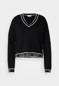 Pull court noir avec encolure en V, manches longues, bordure blanche contrastante le long du col et de l'ourlet, et une ceinture de marque.