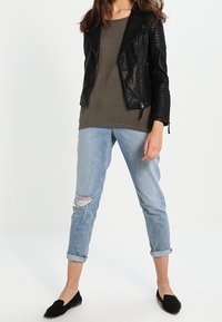 Schwarze Leder-Motorradjacke über einem olivgrünen Hemd, kombiniert mit hochgekrempelten hellblauen distressed Jeans und schwarzen Ballerinas.