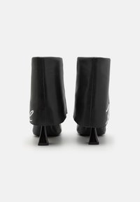 Black leather ankle boots with a high heel, featuring a pointed design and a glossy finish. Edged with a rounded collar. Silver accent detail.