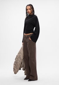 Top negro de manga larga, pantalones anchos marrones y una chaqueta acolchada color marrón claro. El conjunto incluye una parte superior ajustada y un diseño relajado y texturizado.