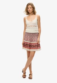 Biały koronkowy top na ramiączkach z dekoltem w szpic, w połączeniu z sukienką w kwiatowy wzór, warstwową, w różowych i czerwonych odcieniach, z koronkowymi wykończeniami.
