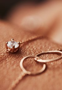 Roze-gouden ketting met een ronde, heldere edelsteen in een zes-kleurige zetting, met een delicate ketting en een zachte ronde sluiting.