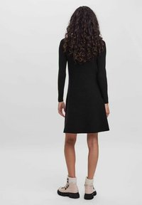 Schwarz, langärmliges Kleid mit ausgestelltem Saum, kombiniert mit beigen Stiefeletten mit schwarzen Sohlen und dekorativen Schnürsenkeln.