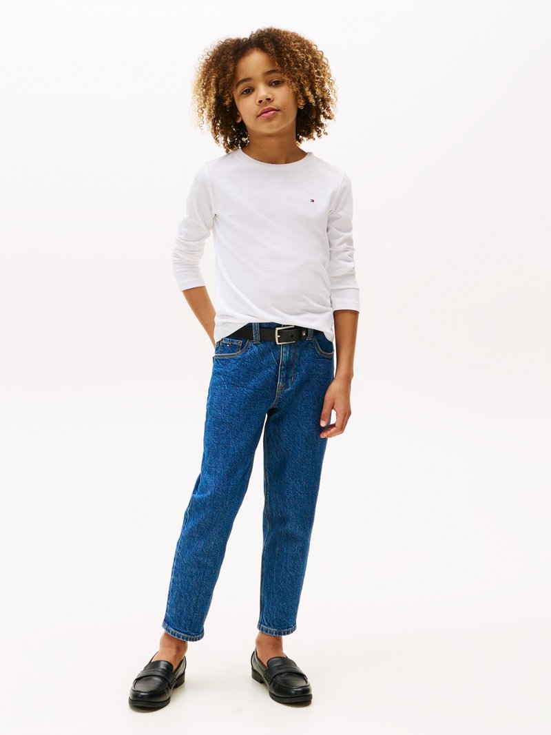 Langermet hvit skjorte, blå teksturerte jeans, svart belte og svarte mokasiner. Barnet poserer med hendene i lommene, og viser frem et avslappet antrekk.