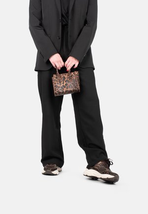 Small brown leopard print handbag held in hands, worn with a black suit and black pants, paired with patterned brown sneakers.